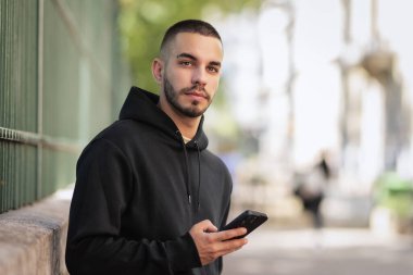 Şehirde sokakta dikilirken yakışıklı bir gencin cep telefonunu kullanırken çekilmiş bir fotoğrafı. Kameraya ve mesaja bakan kendinden emin bir adam.. 