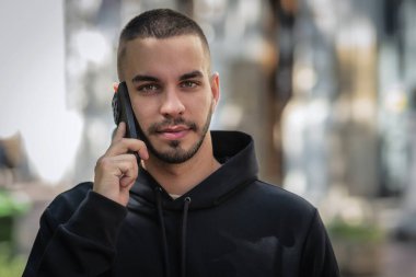 Şehirde sokakta dikilirken yakışıklı bir gencin cep telefonunu kullanırken çekilmiş bir fotoğrafı. Kendine güveni olan kapüşonlu bir adam arıyor..