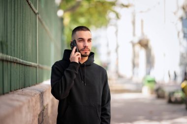 Şehirde sokakta dikilirken yakışıklı bir gencin cep telefonunu kullanırken çekilmiş bir fotoğrafı. Kendine güvenen kapüşonlu bir adam arıyor.. 