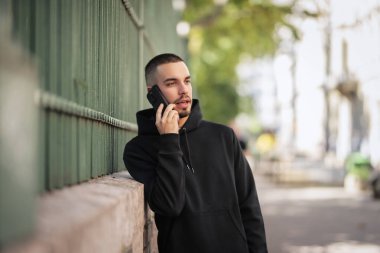 Şehirde sokakta dikilirken yakışıklı bir gencin cep telefonunu kullanırken çekilmiş bir fotoğrafı. Kendine güvenen kapüşonlu bir adam arıyor.. 