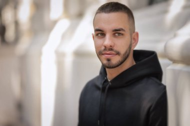 Şehir caddesinde duran şık bir gencin yakın plan portresi. Kapüşonlu genç adam.