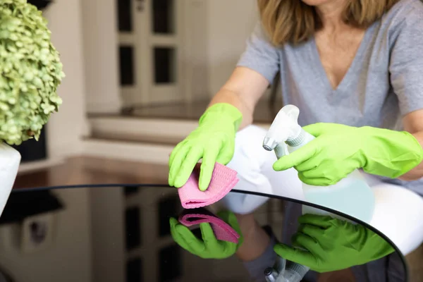 Close-up of a woman\'s hand wiping the coffee table at home. Confident female wearing rubber gloves and using cleaning liquid while cleaning at home.