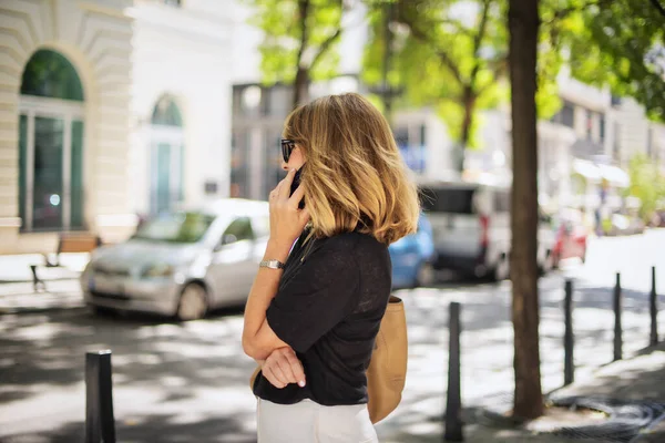 ブロンドの髪を持つ中年の女性は 通りに立って携帯電話を使用しています 自信を持った女性が電話 リアビューショット — ストック写真