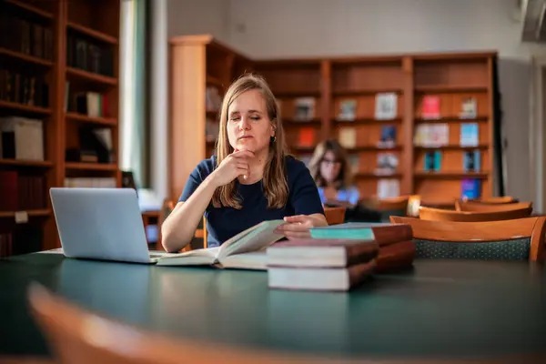 一位视力受损的年轻女子坐在大学图书馆学习 使用笔记本电脑和书籍的年轻女性 图库照片