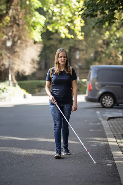 一个带着白色手杖在街上行走的失明女人的画像 一个视力受损的女人穿着休闲装 用手杖穿过街道 全长射击 免版税图库照片