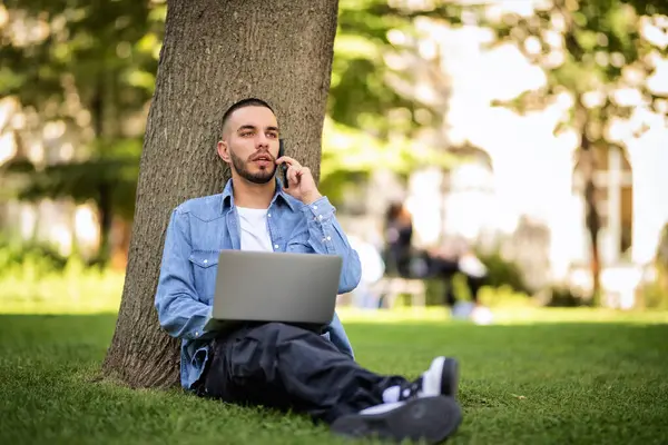 옥외에서 공부하거나 일하기 노트북을 사용하는 젊은이 캐주얼 공원에서 잔디에 스톡 사진