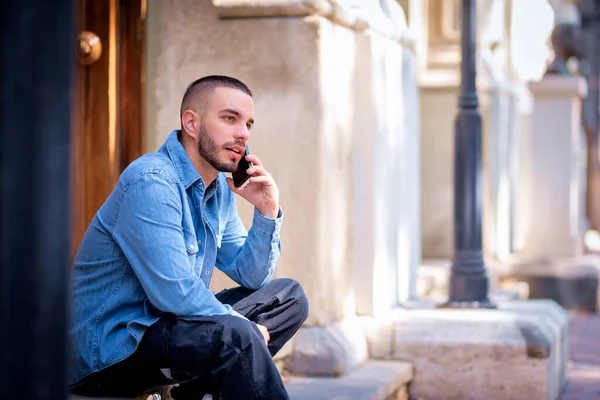 도시의 거리에 앉아있는 자신의 전화를 잘생긴 남자의 스톡 이미지
