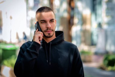 Şehirde sokakta dikilirken yakışıklı bir gencin cep telefonunu kullanırken çekilmiş bir fotoğrafı. Kendine güveni tam bir erkek kapüşonlu giyiyor..