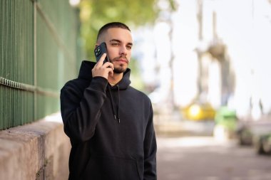 Şehirde sokakta dikilirken yakışıklı bir gencin cep telefonunu kullanırken çekilmiş bir fotoğrafı. Kendine güveni tam bir erkek kapüşonlu giyiyor..