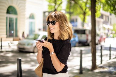 Sokakta yürüyen ve cep telefonunu kullanan çekici orta yaşlı bir kadın. Sarı saçlı bir kadın arıyor..