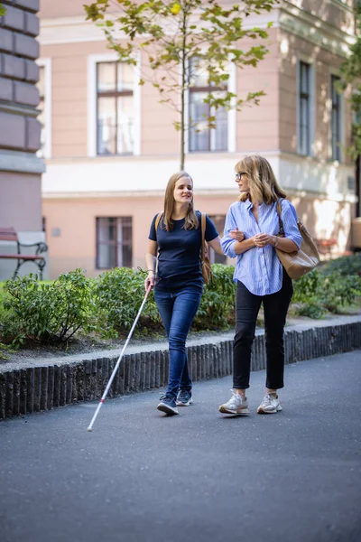 視覚障害のある女性は 街の通りに女性の友人と歩いています 視覚障害者である彼女の友人を支援する成熟した白人女性 全長について ストック画像