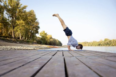 Dışarıda yoga yapan orta yaşlı bir adam. Kafkasyalı adam yoga minderi kullanıyor ve doğada yoga yapıyor. Yoga amuda kalkıyor..