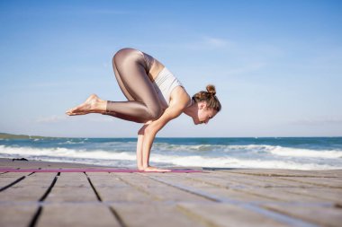 Nehre bakan karga pozu veren genç bir kadın. Nehir kenarındaki iskelede yoga yapan bir kadın yoga koçu..