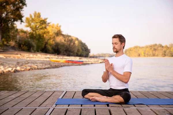 整整一个高加索人在一个又一个湖边的码头上练习瑜伽 成熟男子做莲花姿势 手牵手祷告姿势 — 图库照片