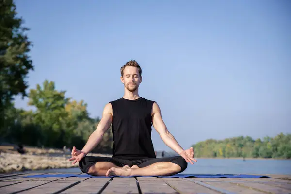 整整一个高加索人在一个又一个湖边的码头上练习瑜伽 成熟的男子在蓝天的衬托下练习莲花姿势 — 图库照片
