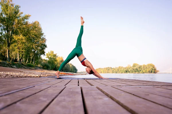 一个女人在河边的码头上练瑜伽 运动女士在瑜伽垫上伸展和热身 图库图片