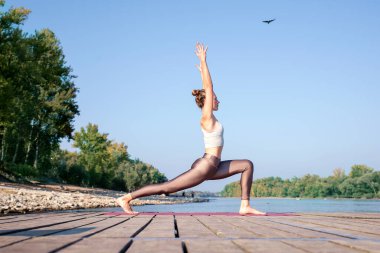 Nehir kenarındaki iskelede yoga yapan beyaz bir kadın. Çekici kadın sarı saçlı ve gülümseyen.. 