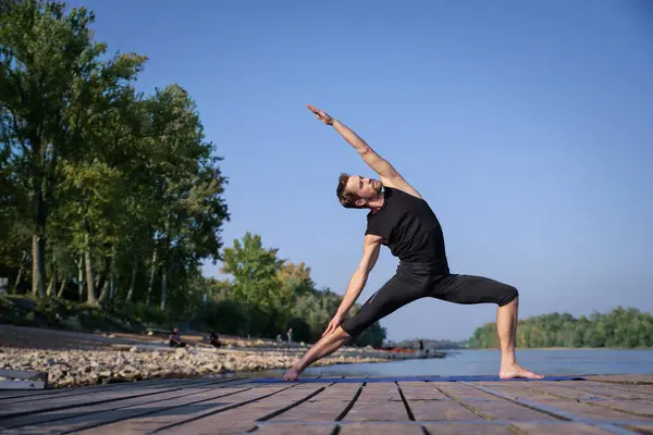 全长的高加索男子在一个又一个湖边的码头上练习瑜伽 免版税图库照片