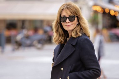 Şehir caddesinde yürüyen orta yaşlı güzel bir kadın. Sarı saçlı, mavi ceketli ve güneş gözlüklü bir kadın.. 