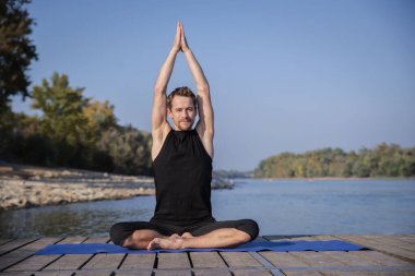 Orta yaşlı bir adam dışarıda yoga yapıyor. Kafkasyalı adam yoga minderi kullanıyor ve esniyor.. 