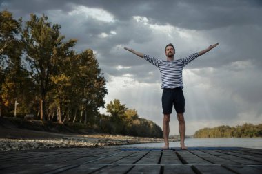 Dışarıda yoga yapan orta yaşlı bir adam. Beyaz adam yoga minderi ve güneş selamı kullanıyor.. 