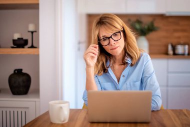 Orta yaşlı bir kadının evde oturup iş için dizüstü bilgisayar kullandığını düşünmek. Merkez ofis. Kendine güvenen iş kadını internet konferansı yapıyor ya da internette geziniyor.. 