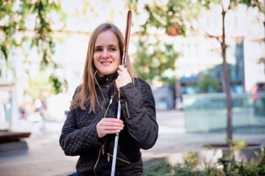 Beyaz baston tutan ve şehirde bir bankta oturan görme engelli bir kadının yakın çekimi.. 