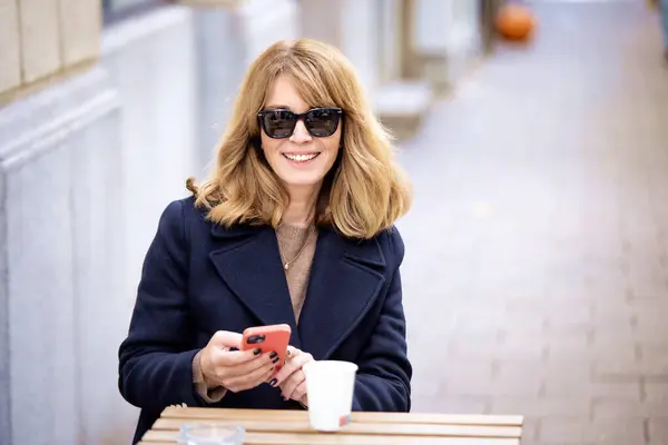 Mujer Sentada Una Mesa Frente Café Usando Teléfono Inteligente Mientras —  Fotos de Stock