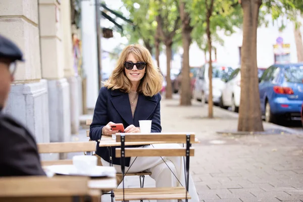 Mulher Sentada Uma Mesa Fora Café Usando Seu Smartphone Enquanto Fotografias De Stock Royalty-Free