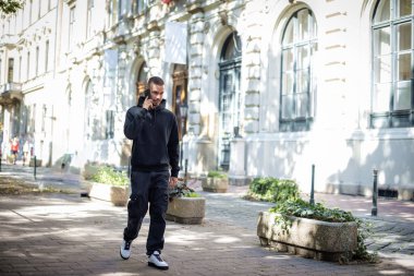 Şehir caddesinde yürüyen ve akıllı telefon kullanan genç bir adam. Kapüşonlu, yakışıklı, beyaz bir adam arıyor.. 