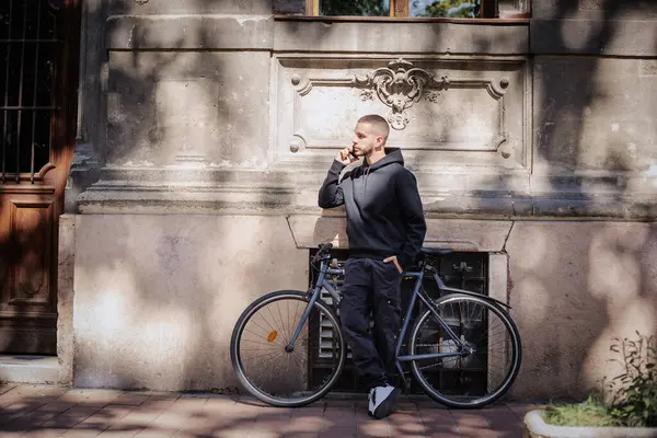 全长的年轻人站在他的自行车旁边的大楼前 打电话给他 英俊的高加索男人穿着休闲装 — 图库照片