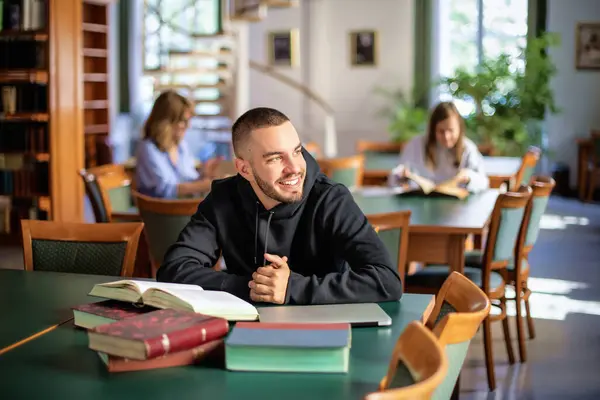 自信的年轻人坐在大学的图书馆里学习 白种人学生穿着休闲装 望着远方 — 图库照片