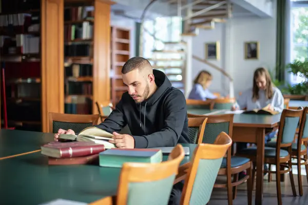 Självsäker Ung Man Sitter Universitetsbiblioteket Och Läser Bok Stilig Student Stockfoto