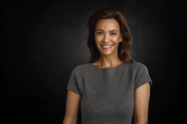 Stüdyo portresi, gri elbiseli esmer bir kadının izole edilmiş koyu arkaplanda gülümsemesi. Boşluğu kopyala. 