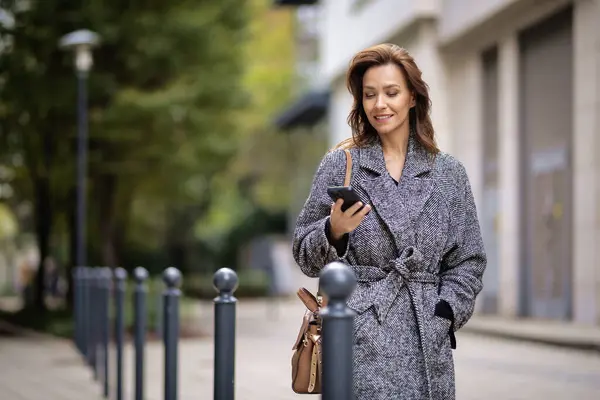 迷人的女人走在街上 用智能手机 穿着冬衣和发短信的中年女性 — 图库照片