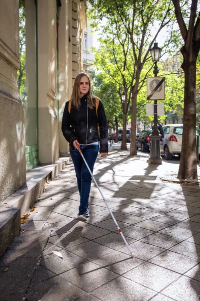 街の道路を横断する白い杖を持つ盲目の女性の肖像画 視覚障害のある女性がカジュアルな服を着て 道を渡るために杖を使った 全長ショット — ストック写真