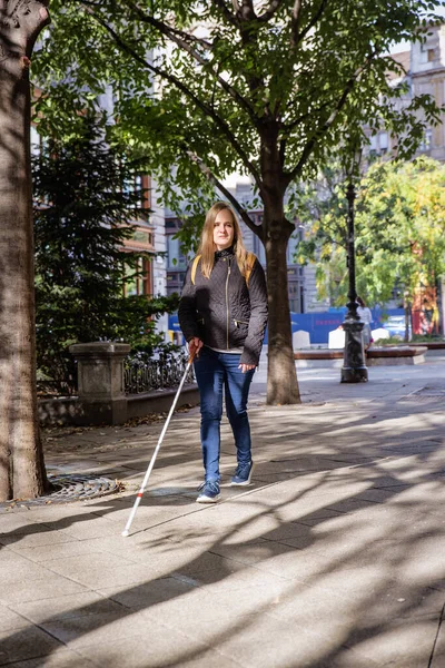 街の道路を横断する白い杖を持つ盲目の女性の肖像画 視覚障害のある女性がカジュアルな服を着て 道を渡るために杖を使った 全長ショット — ストック写真