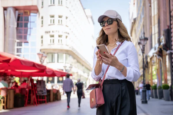 Close-up of an attractive woman wearing smart clothes and sunglasses while walking in a city and speaking on her mobile phone.