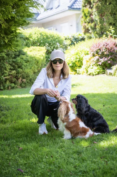 Bahçede sevimli yavrularıyla oturan gülümseyen kadın. Beyzbol şapkası ve güneş gözlüğü takan gülümseyen bir kadın. Tam boy çekim.