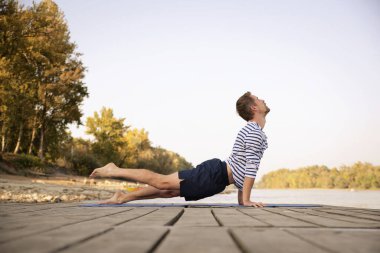 Dışarıda yoga yapan orta yaşlı bir adam. Kafkasyalı adam yoga minderi kullanıyor ve doğayı geriyor..