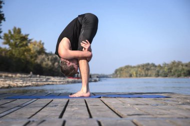 Dışarıda yoga yapan orta yaşlı bir adam. Kafkasyalı adam yoga minderi kullanıyor ve doğayı geriyor..