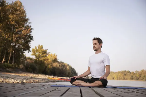 Middle aged man practicing yoga outdoor. Caucasian man using yoga mat and doing lotus pose on nature.