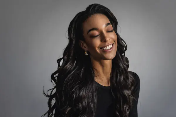アフリカ系アメリカ人の女性の肖像画を元気な笑顔に 灰色の背景に対して目を閉じた黒い長髪の女性 コピースペース — ストック写真