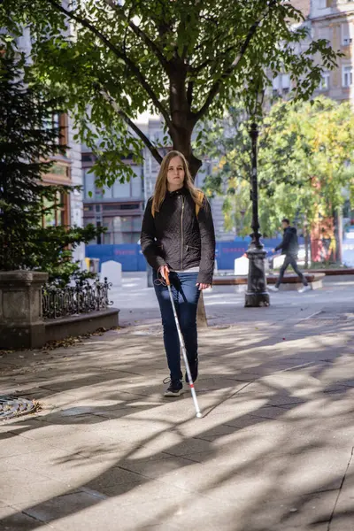 Blind woman with white cane walking in the city. A visually impaired woman wearing casual clothes and using her cane to cross the street.