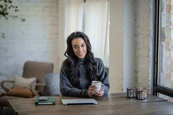 Pencerenin yanındaki masada oturan ve dizüstü bilgisayarı üzerinde çalışan Afro-Amerikalı bir kadın. Merkez Ofis.