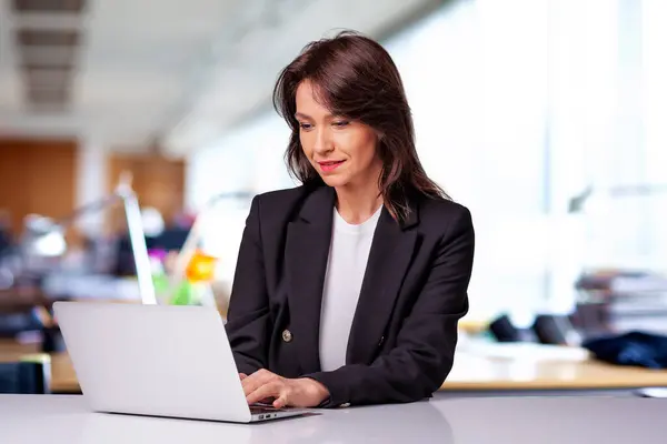 迷人的女商人穿着西装 工作时使用笔记本电脑 笑着坐在办公室里工作的女人 图库图片