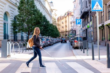 Şehirde yoldan karşıya geçen beyaz bastonlu kör bir kadının portresi. Sıradan kıyafetler giyen ve sopasıyla karşıya geçen görme engelli bir kadın. Tam boy çekim. 
