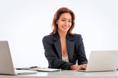 Orta yaşlı bir iş kadını izole edilmiş arka planda masa başında oturuyor. İş için dizüstü bilgisayar kullanan kendine güvenen profesyonel bir kadın. Boşluğu kopyala. 