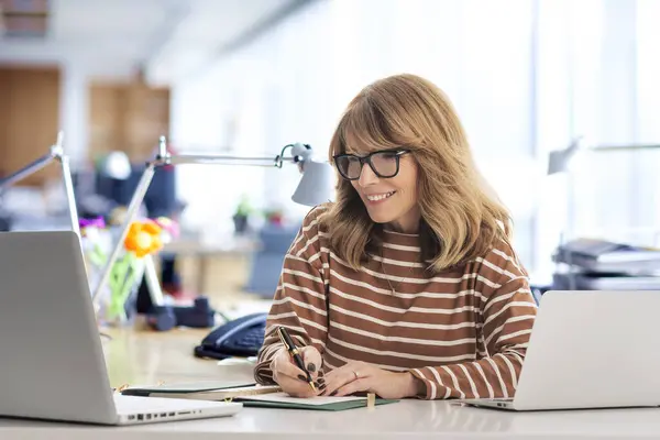 一位中年女商人坐在办公室的办公桌前 自信的职业女性使用笔记本电脑工作 复制空间 免版税图库照片