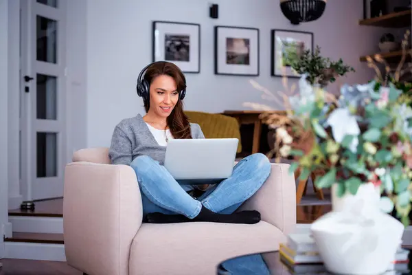 インターネットで閲覧している間 ノートパソコンを使用してヘッドフォンを持つ美しい中年女性の全長 ホームオフィス ストックフォト